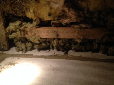 Underneath insulation showing wooden beam and wall.