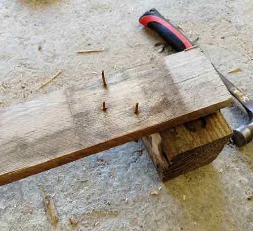 Knocking old nails back through pallet slats to remove them