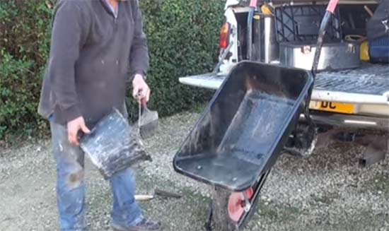 Slopping water from a bucket over a wheelbarrow to clean it